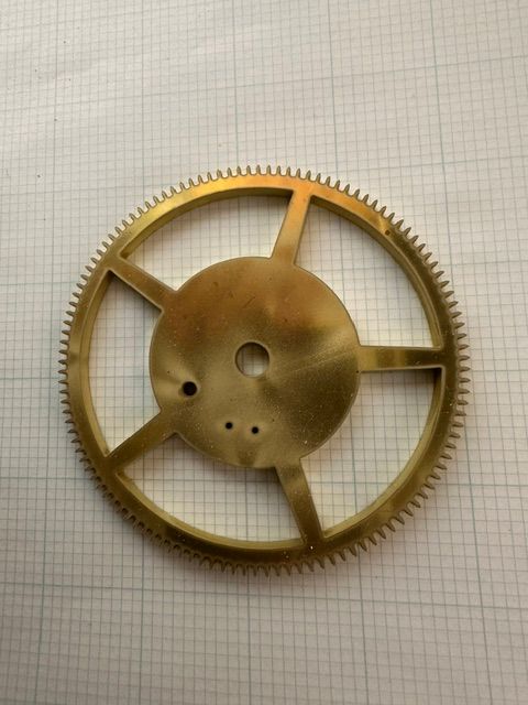 Brass gear wheel with spokes and a central hub on graph paper background
