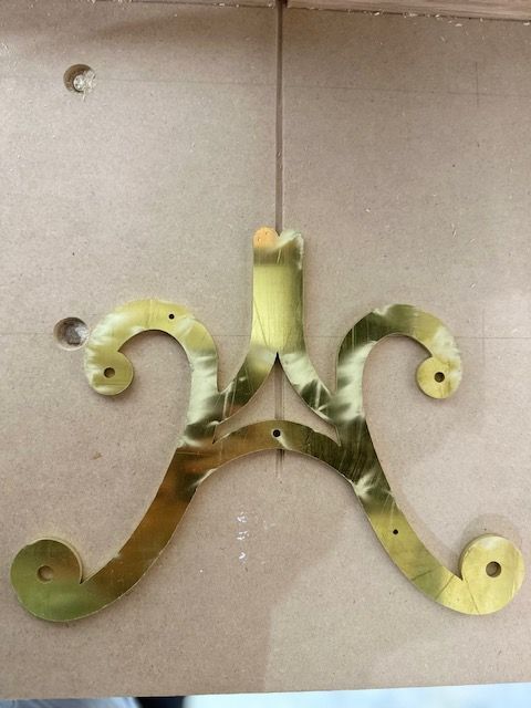 Green metal ornamental wall bracket with curled ends mounted on a beige wall