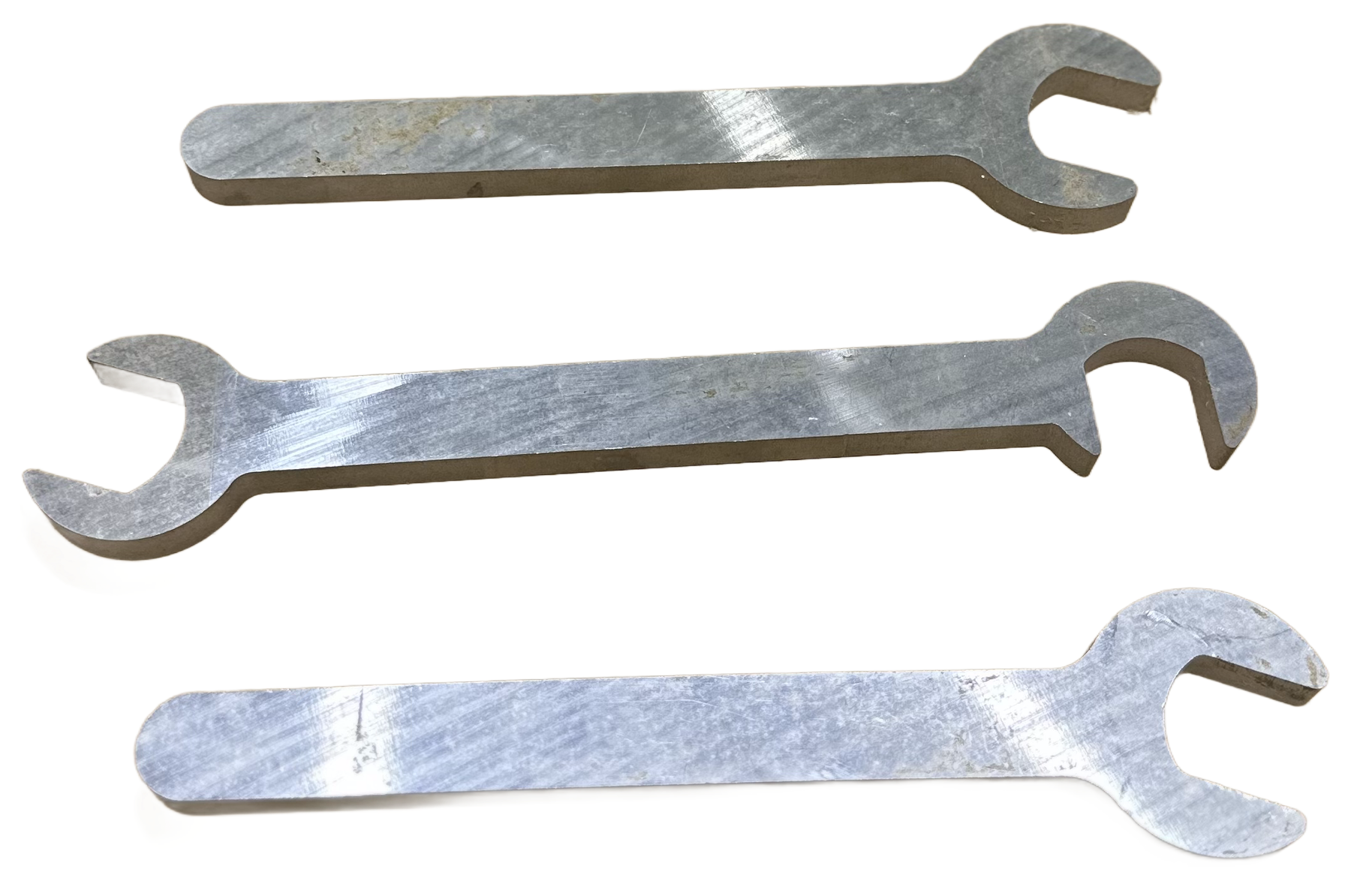 Three silver metal open-end wrenches of different sizes resting on a wooden surface.