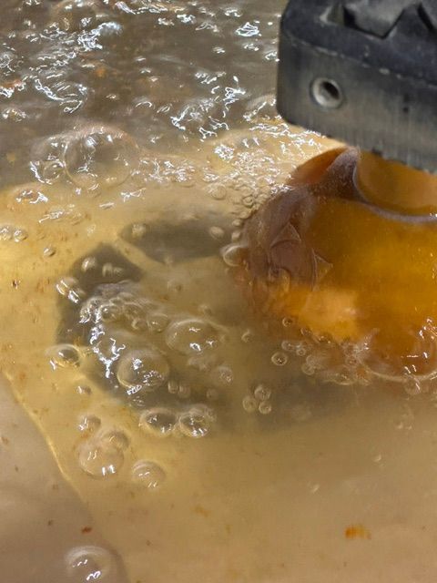 Orange utensil mixing foamy batter in a bowl of bubbling liquid