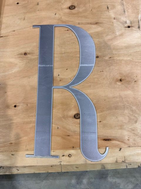 Silver letter “R” mounted on a wooden wall.
