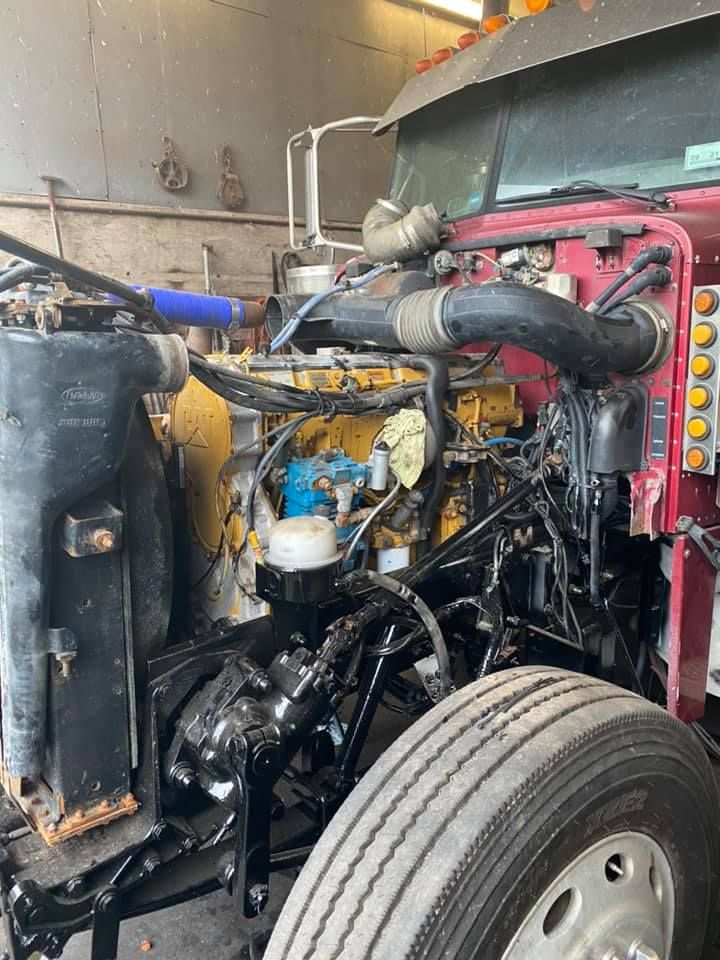 Semi-truck engine bay, red chassis, black engine, yellow components, blue hoses, tire visible.