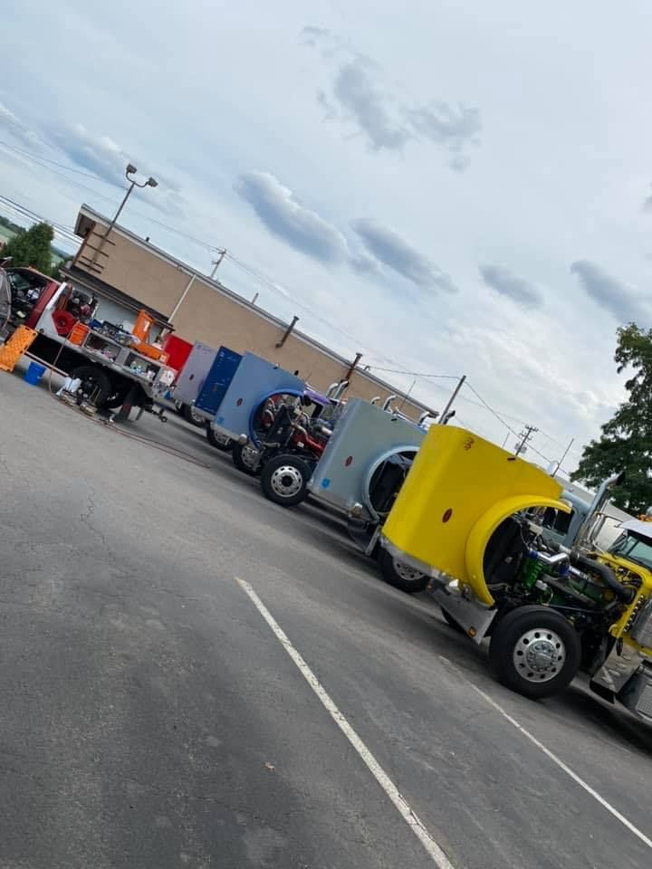 Trucks parked with their hoods up, revealing engine parts. Cloudy sky overhead.