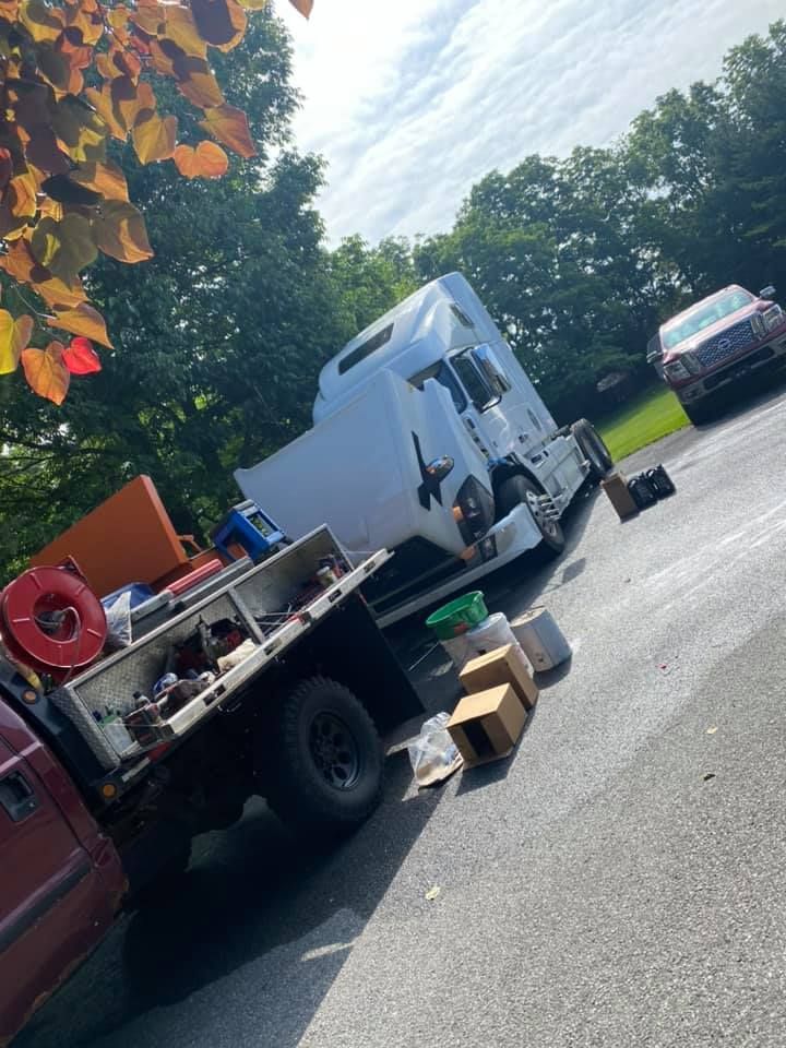 A red truck bed with a white truck cab, boxes, and tools sits on asphalt, with trees and a car in the background.