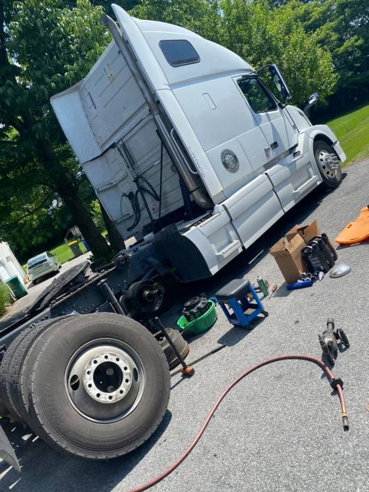 A white semi-truck with a flat tire parked on a driveway; repair tools scattered nearby.