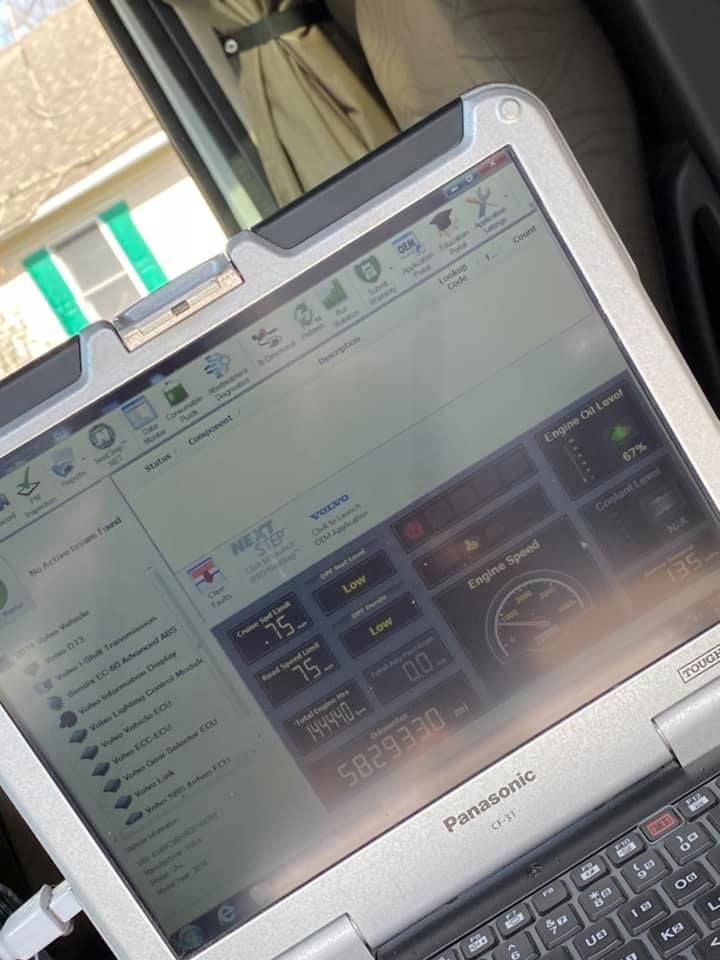 Laptop displaying vehicle diagnostics in a car. Gauges visible. Sunlight on screen.