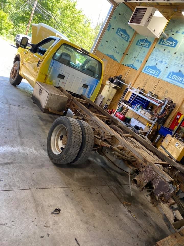 Yellow Ford truck chassis in a garage, with cab and dual rear wheels.