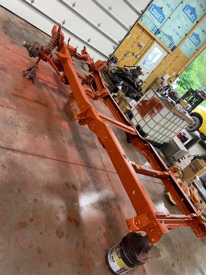 Orange-painted car chassis in a workshop with tools and parts scattered around.