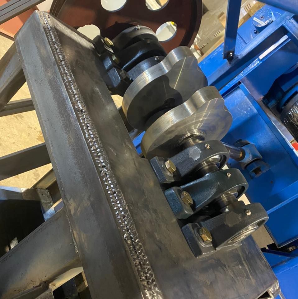 A metal crankshaft mounted on a blue machine frame with weld lines visible.