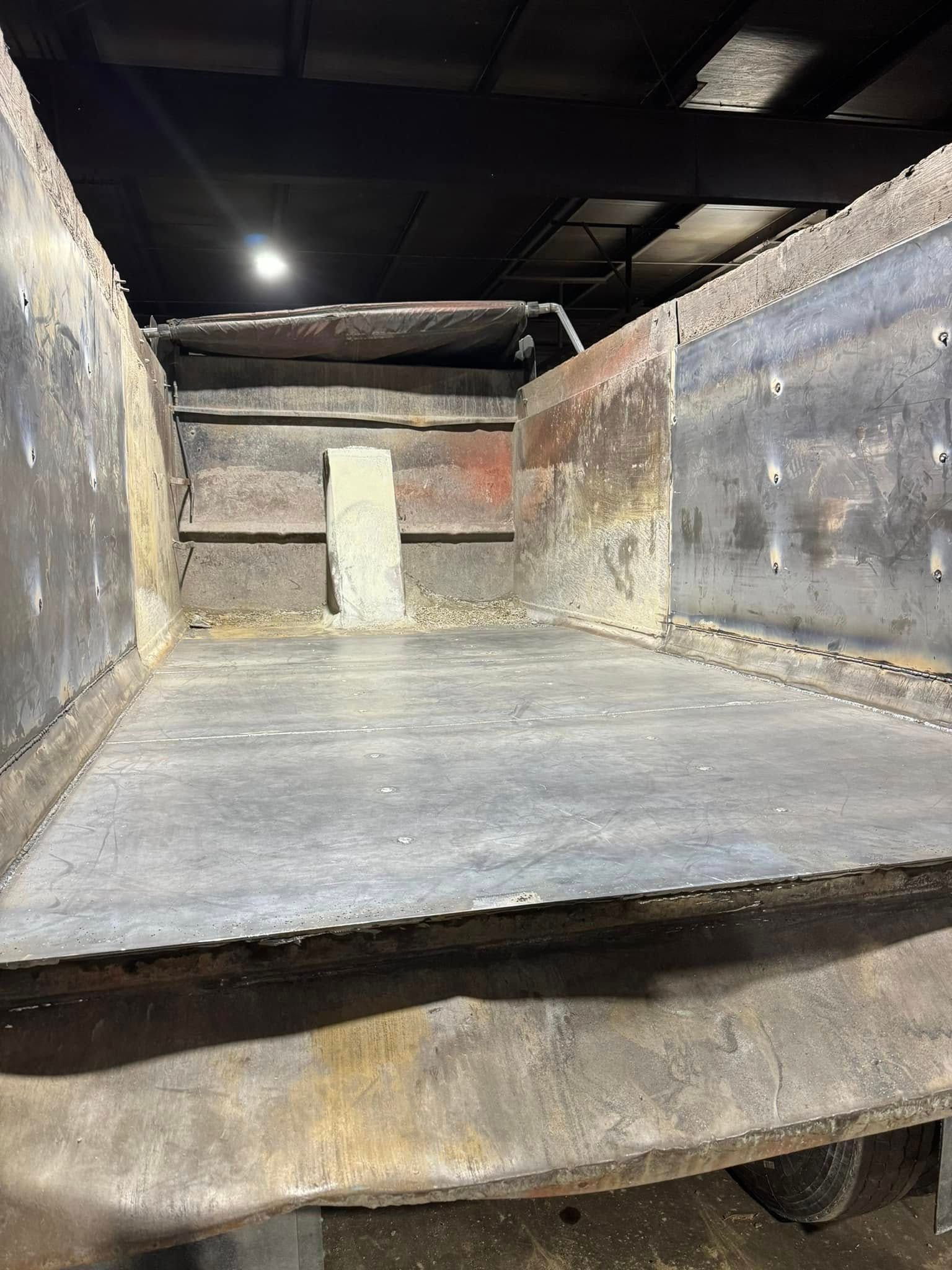 Empty, rusty metal dump truck bed with a grey floor and walls.