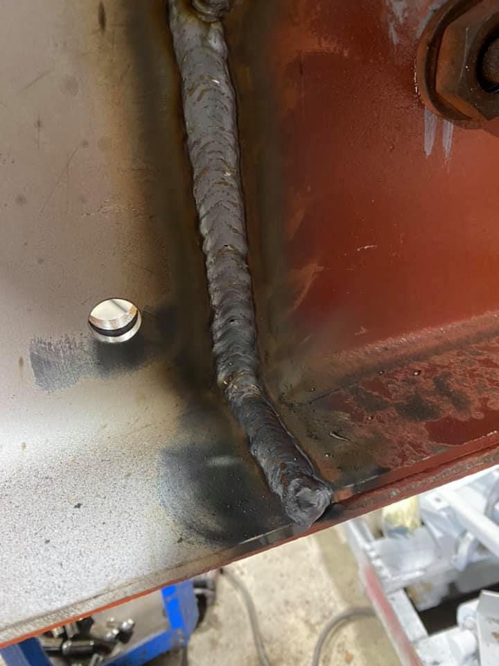 Close-up of a welded metal joint on red painted steel. Dark weld bead joins two pieces.