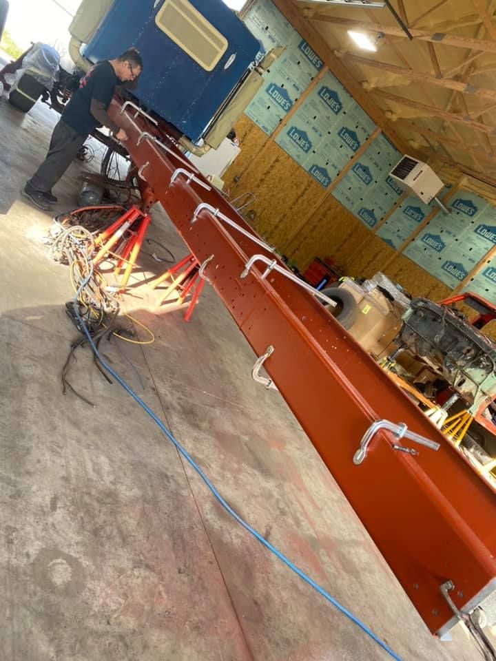 Man working on a truck; long, orange metal piece with curved hooks; in a garage setting.