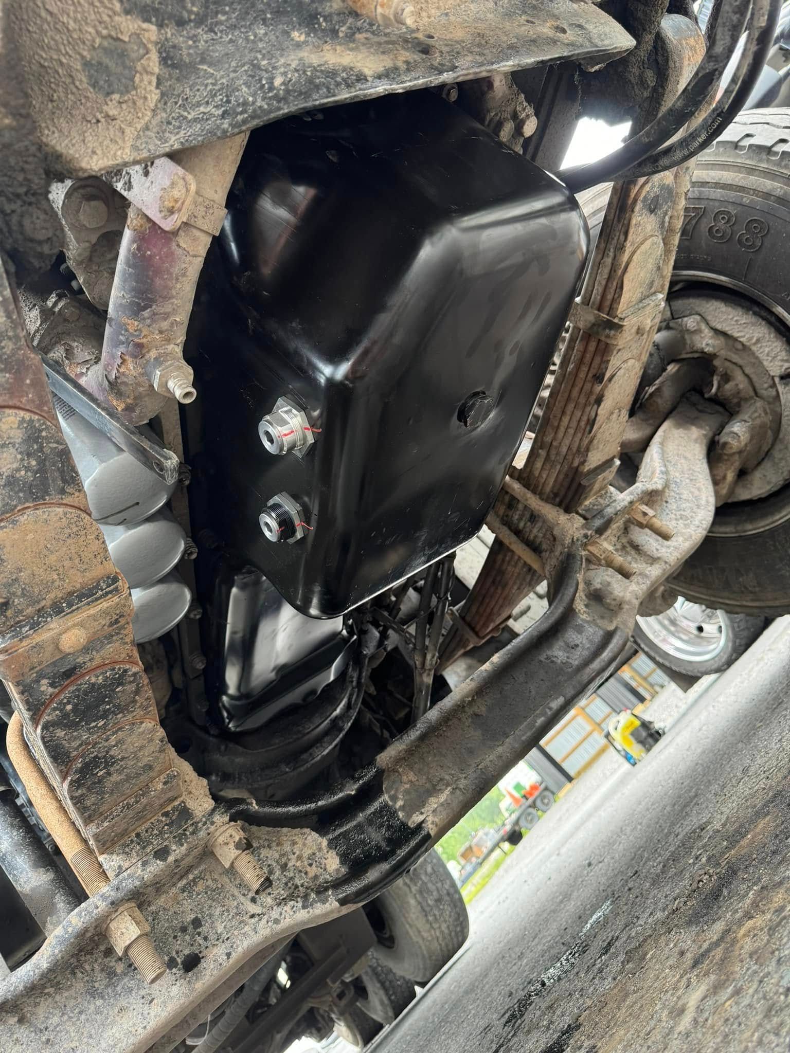 Underside of a black box attached to vehicle chassis, showing suspension and axles.
