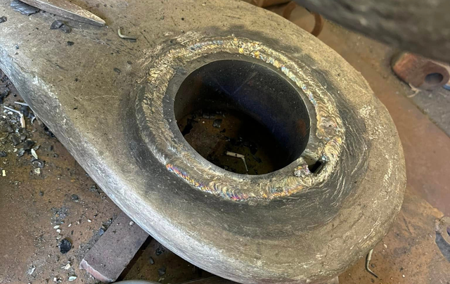 Overhead view of a dirty, gray metal object with a large circular hole and welded edges.