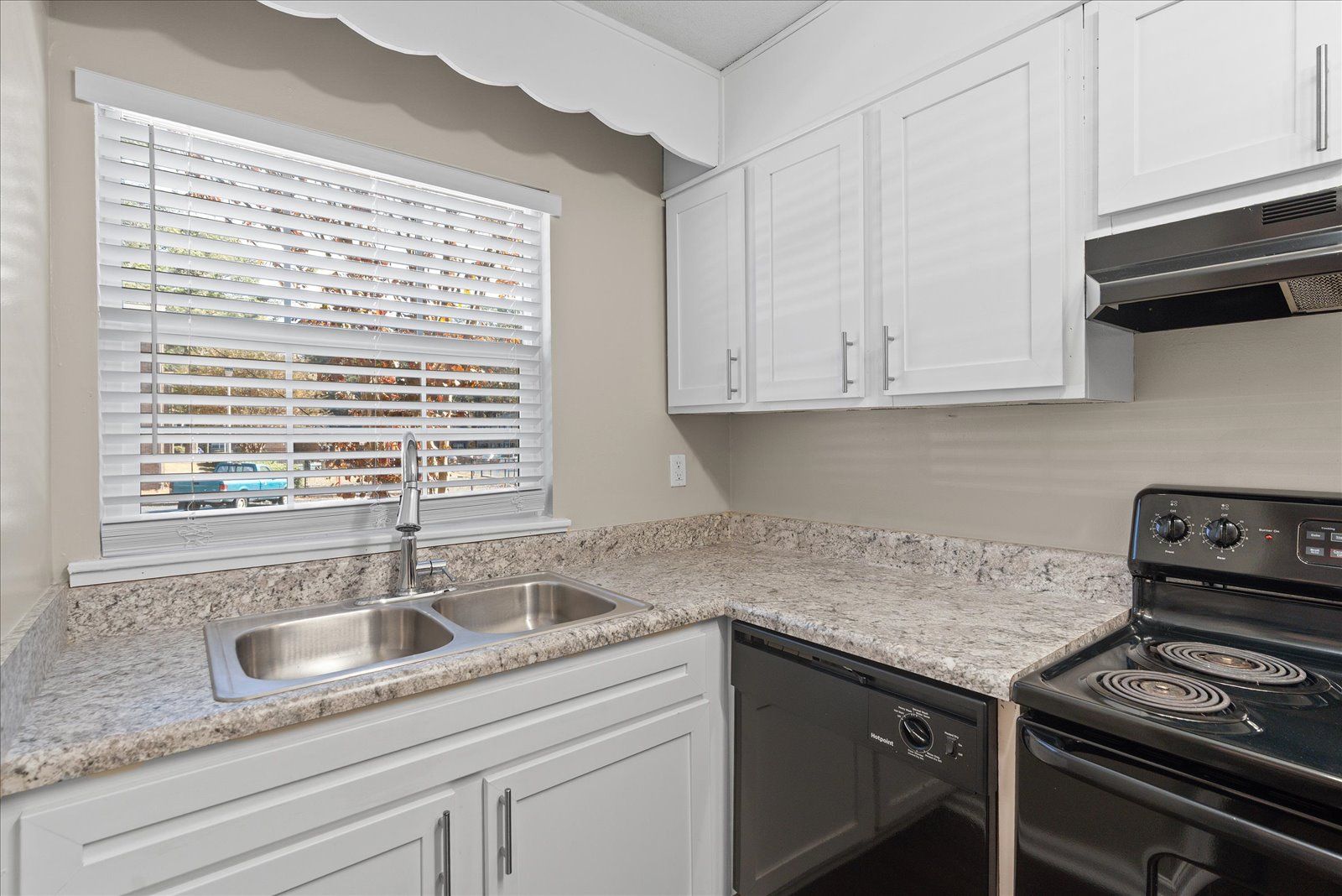 A kitchen featuring white cabinets, speckled granite countertops, a double-basin sink, and a black stove.