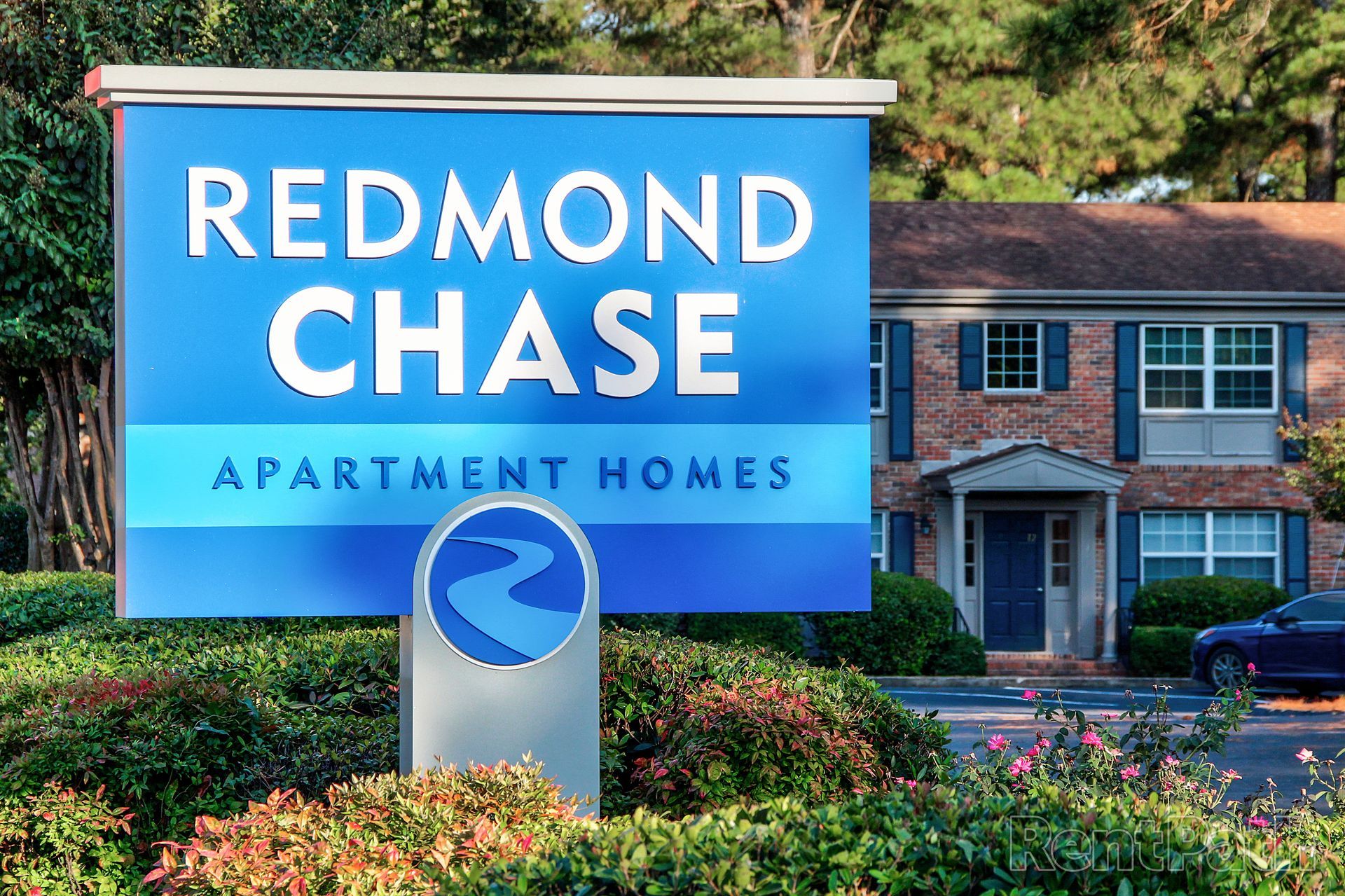 A blue and white Redmond Chase Apartment Homes sign stands in front of a brick building with dark blue shutters.