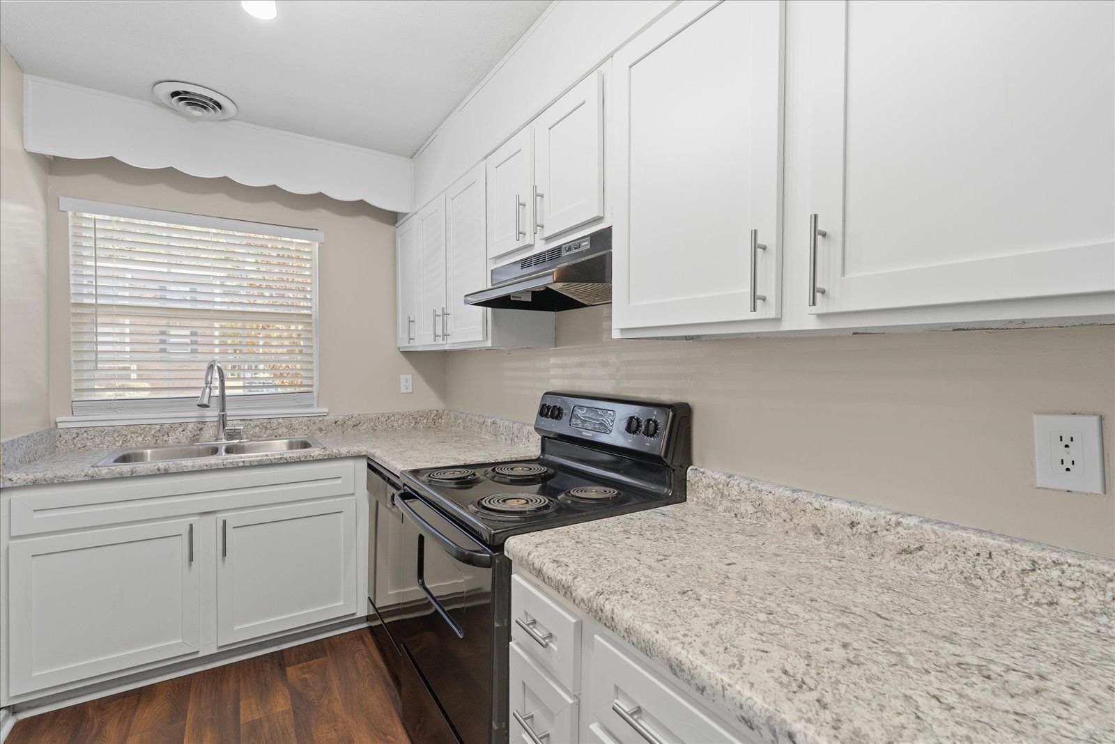A kitchen featuring white cabinets, speckled countertops, a dark stove, and a window above the sink.
