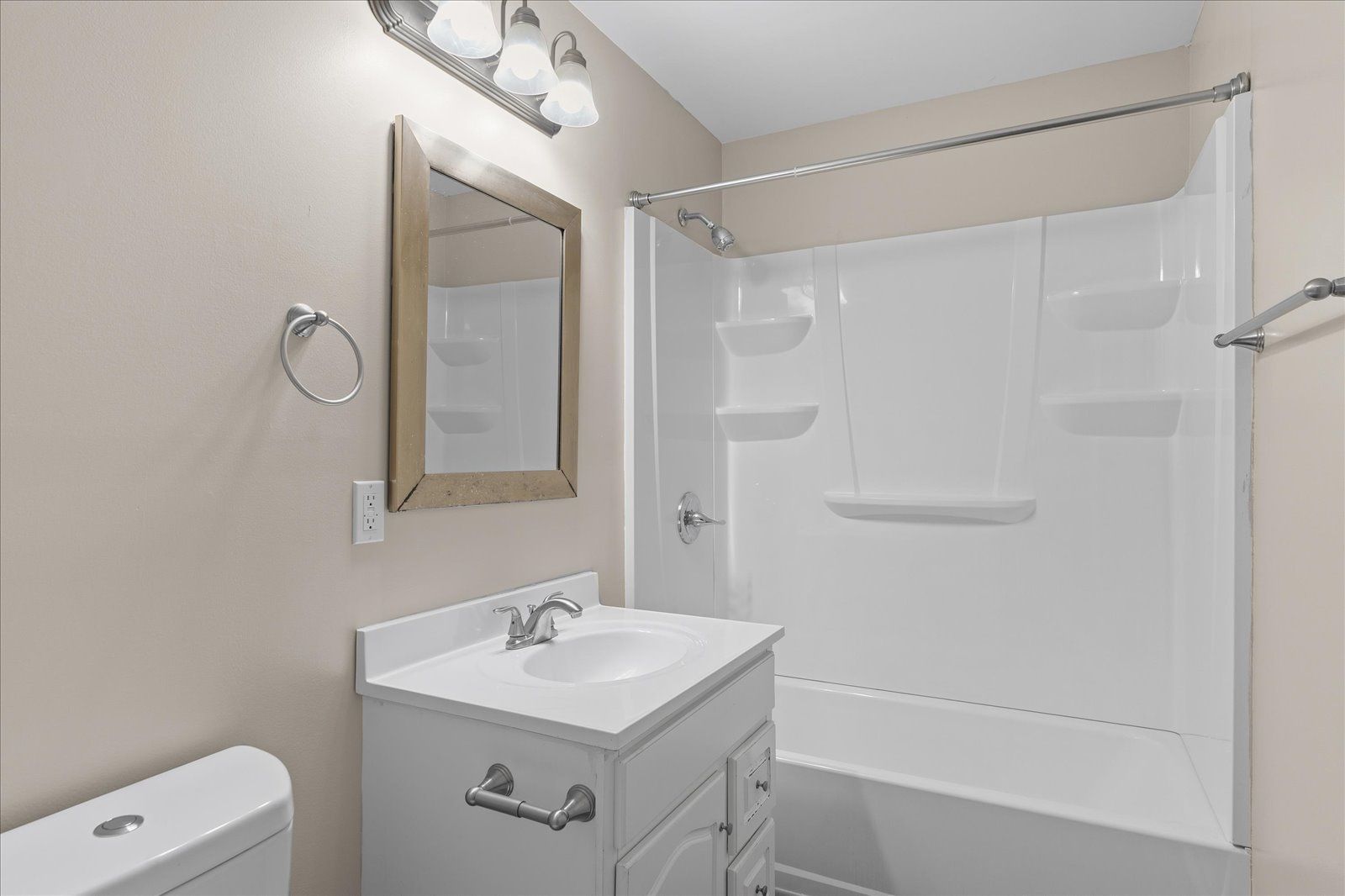 A modern bathroom featuring a white vanity with a sink, a wood-framed mirror, a toilet, and a white tub-shower unit.