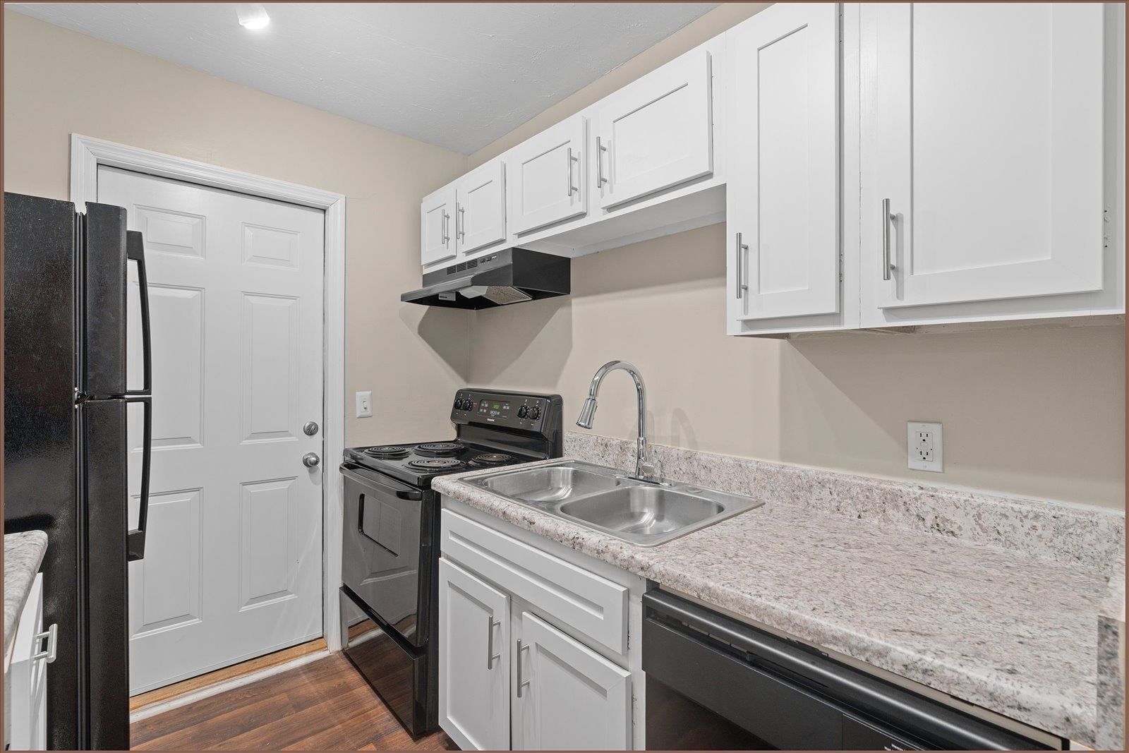 A kitchen with white cabinets, speckled countertops, a black stove and refrigerator, and a door leading outside.