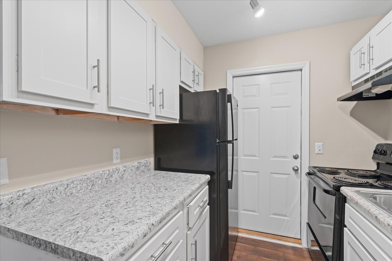A kitchen featuring white cabinets, speckled granite countertops, a black refrigerator, and a white door.