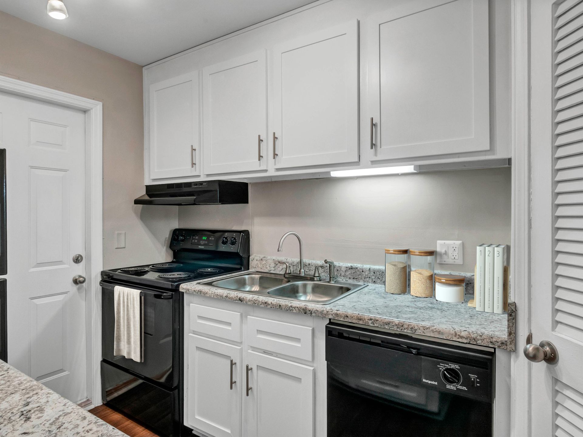 A modern kitchen with white cabinets, speckled countertops, a black stove, and a black dishwasher.