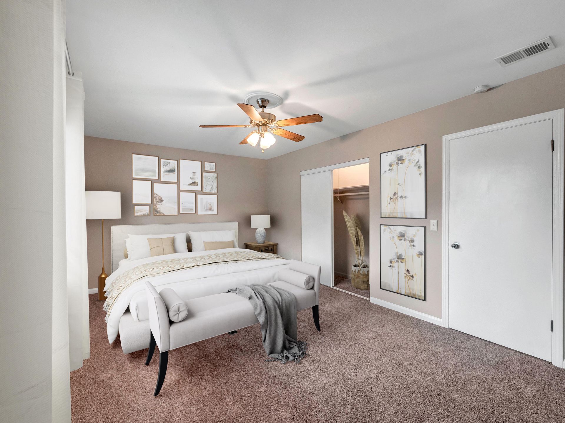 A bedroom with a queen bed, gray carpet, beige walls, a white ceiling fan, and framed art on the wall.