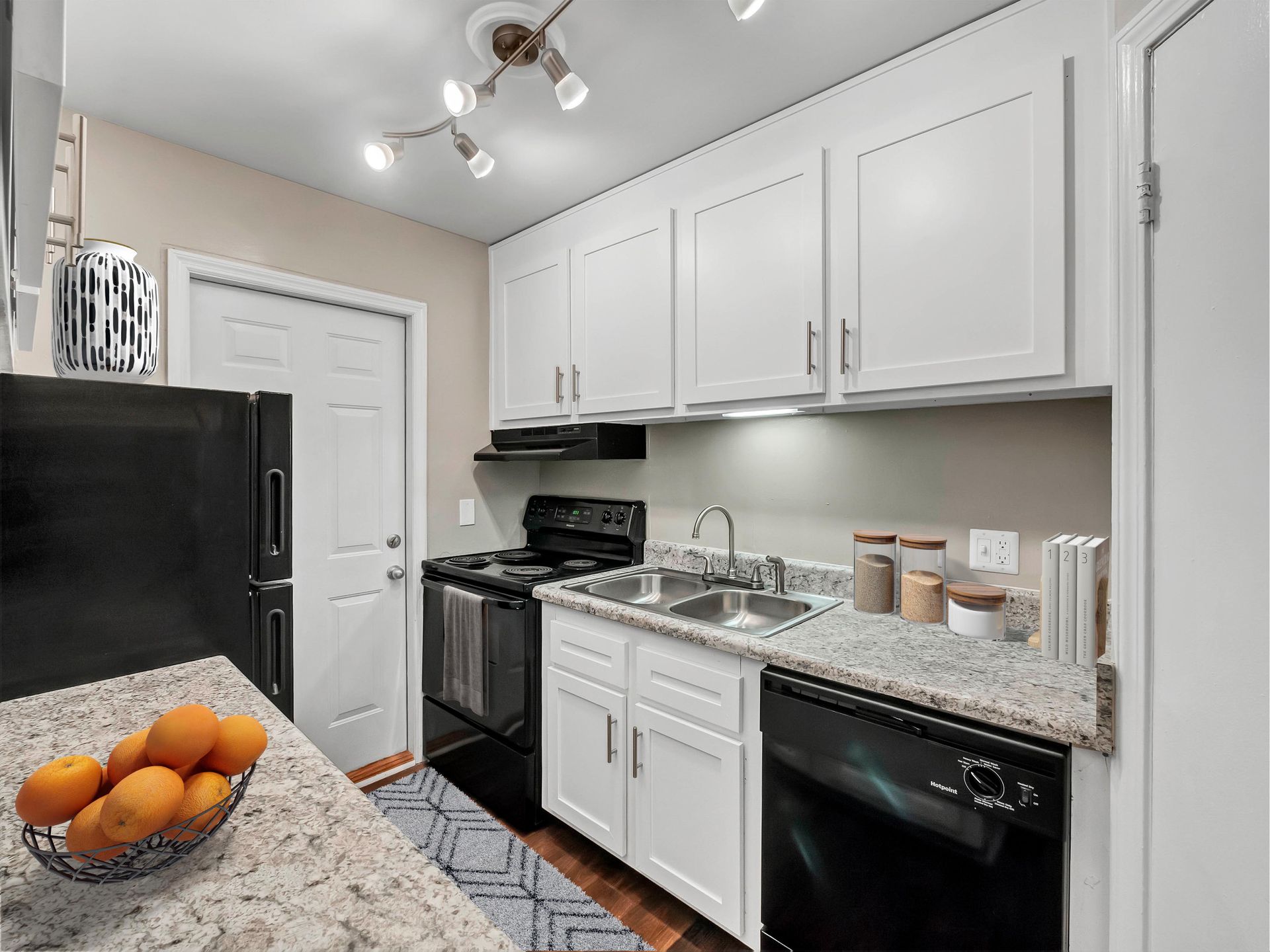 A kitchen with white cabinets, granite countertops, a black stove and dishwasher, and a bowl of oranges on the counter.