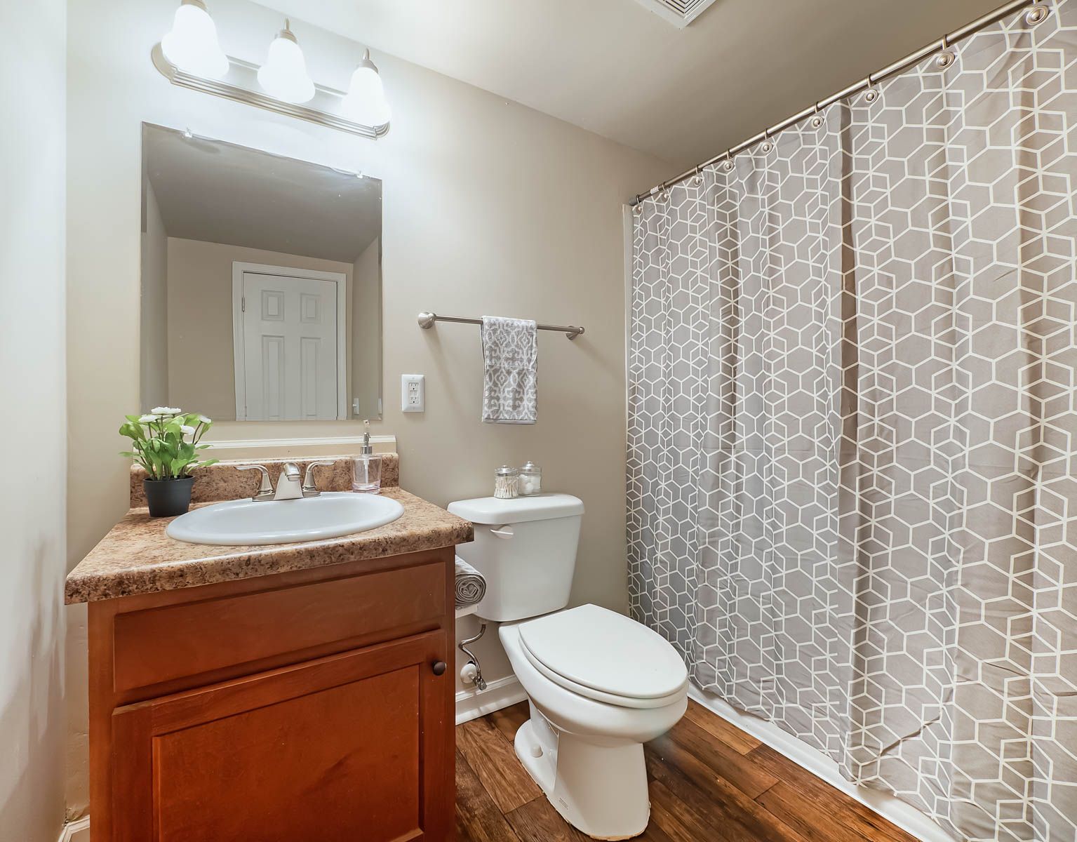A small bathroom with a wooden vanity, white toilet, patterned shower curtain, and a mirror above the sink.