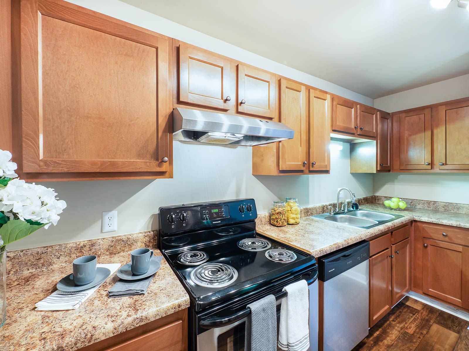 A kitchen with light wood cabinets, granite countertops, a black electric stove, and a stainless steel dishwasher.