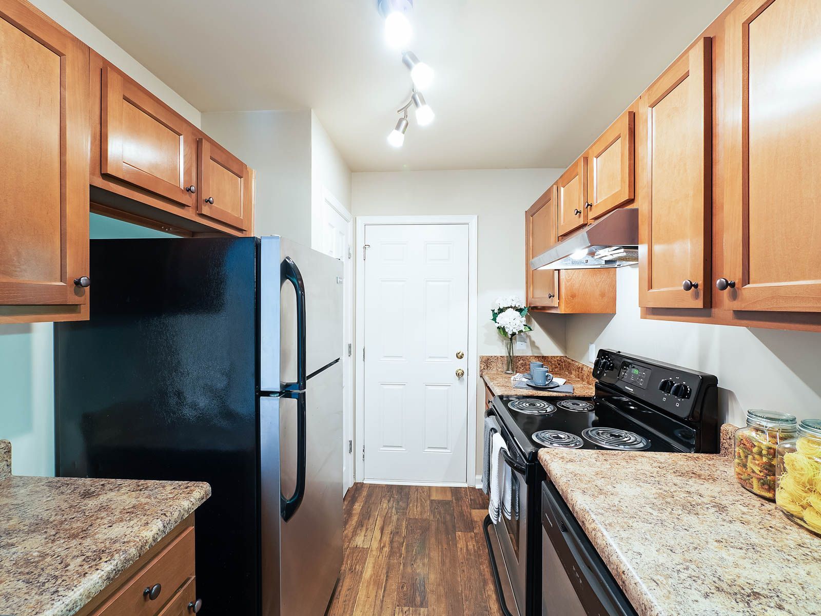 A galley kitchen with light wood cabinets, speckled laminate countertops, a black refrigerator, and a black stove.