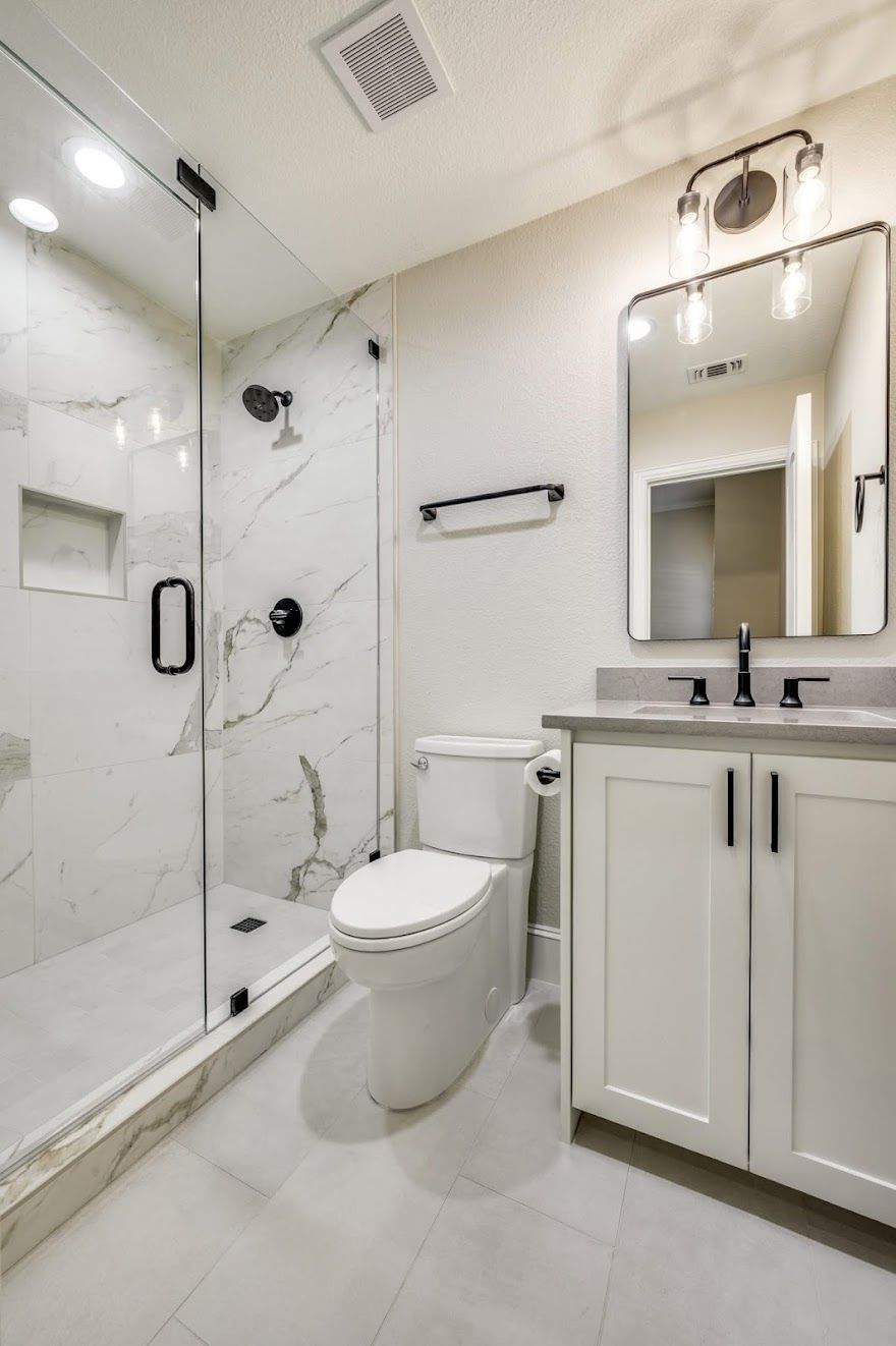 Modern bathroom featuring a glass walk-in shower with white marble walls, a white toilet, and a vanity with a mirror.