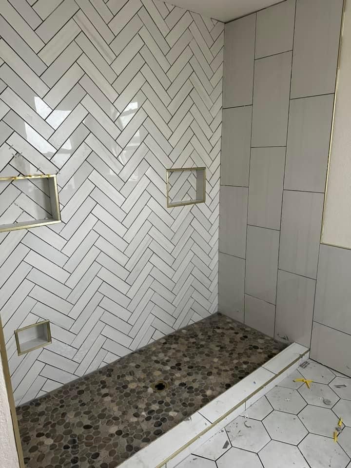 A modern shower with white herringbone wall tiles, gray rectangular side tiles, and a dark stone pebble floor.