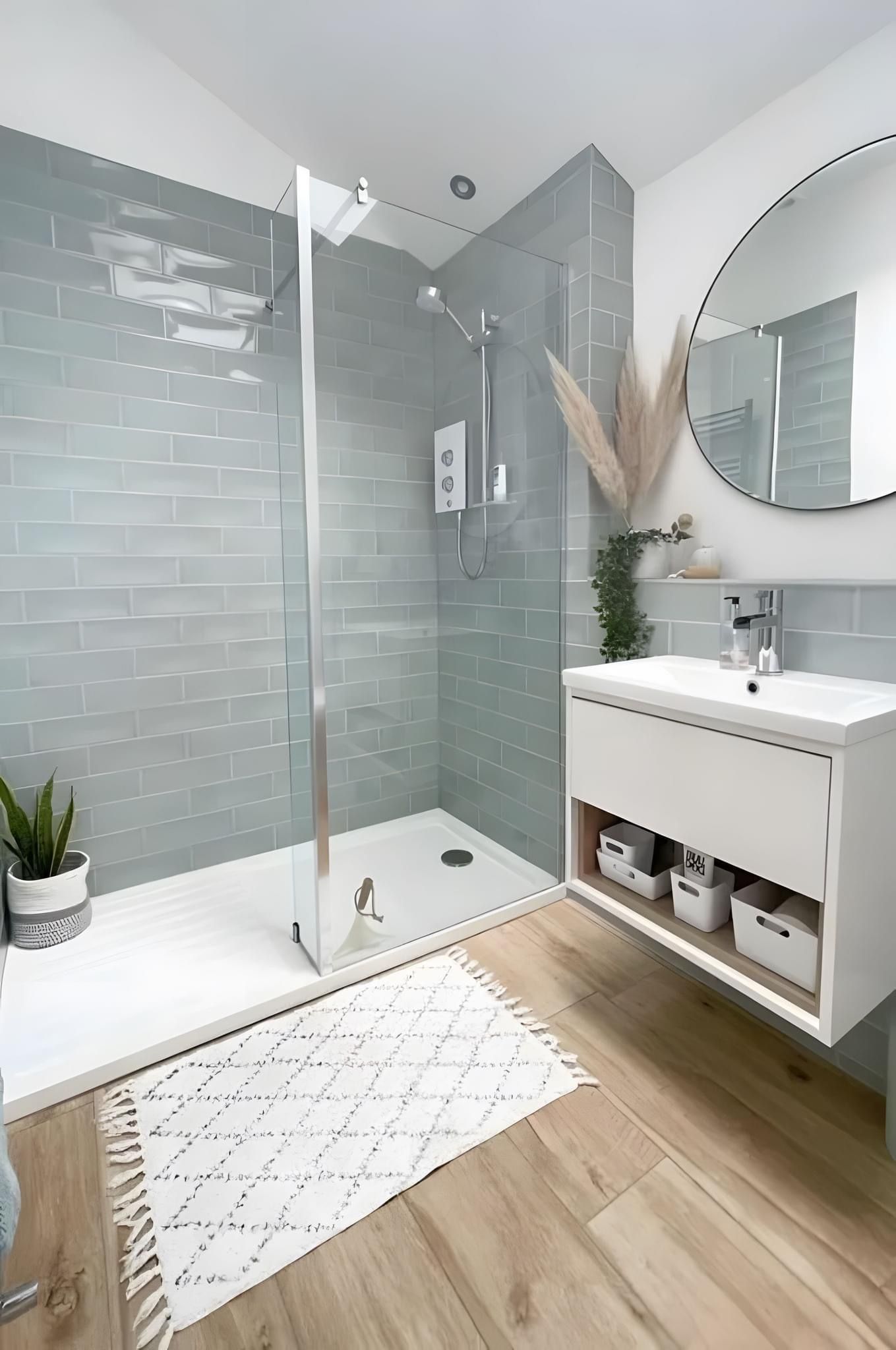 A modern bathroom with a walk-in shower featuring blue-grey tiled walls, a white vanity, and a light wood-look floor.