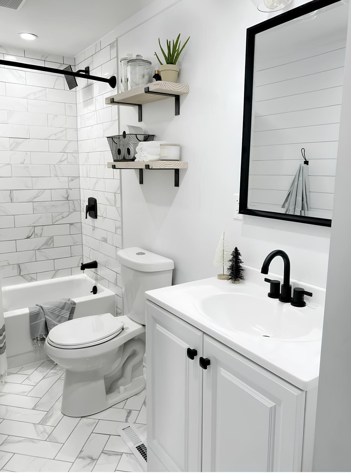A modern bathroom with a white vanity, black faucet, toilet, bathtub with white tiled walls, and two wooden wall shelves.