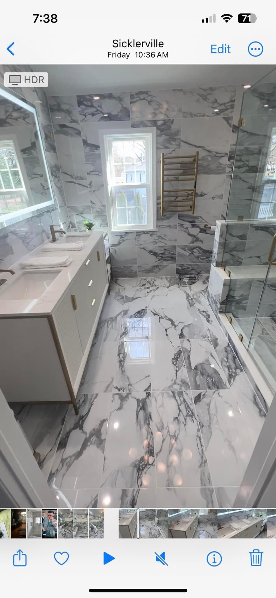 A modern bathroom with white marble tile walls and floors, a double vanity, a large illuminated mirror, and a walk-in shower.