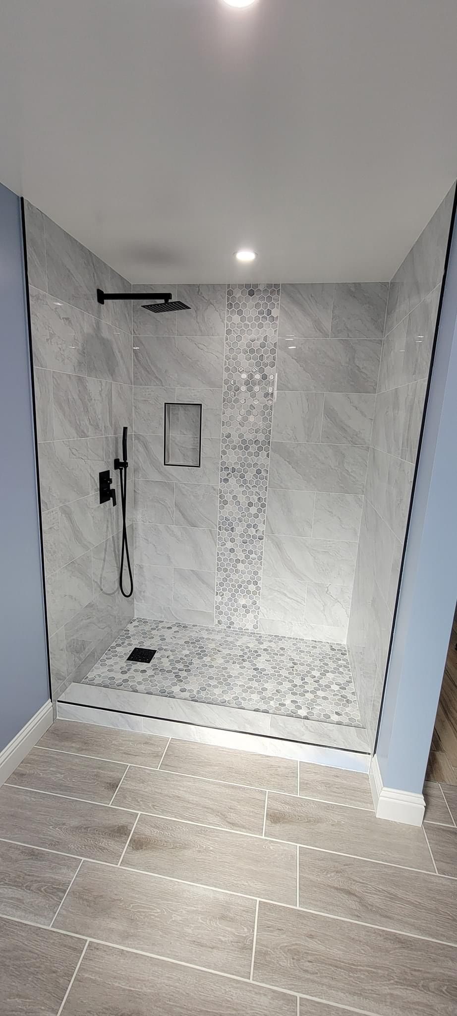 Modern shower with marble-look wall tiles, a decorative mosaic vertical stripe, and matte black fixtures.