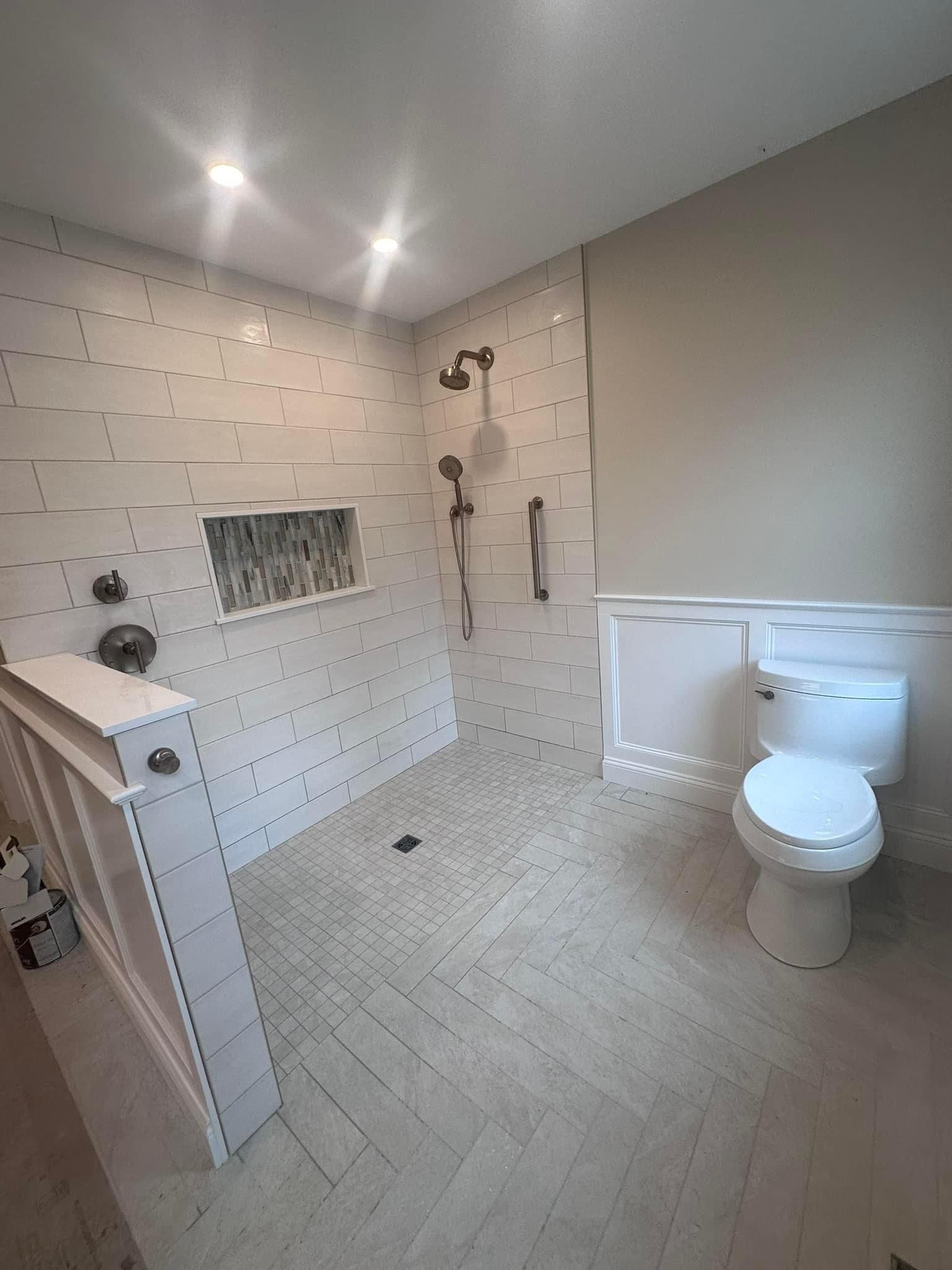 A modern bathroom featuring a walk-in shower with white tile, a niche, and a separate white toilet against a neutral wall.