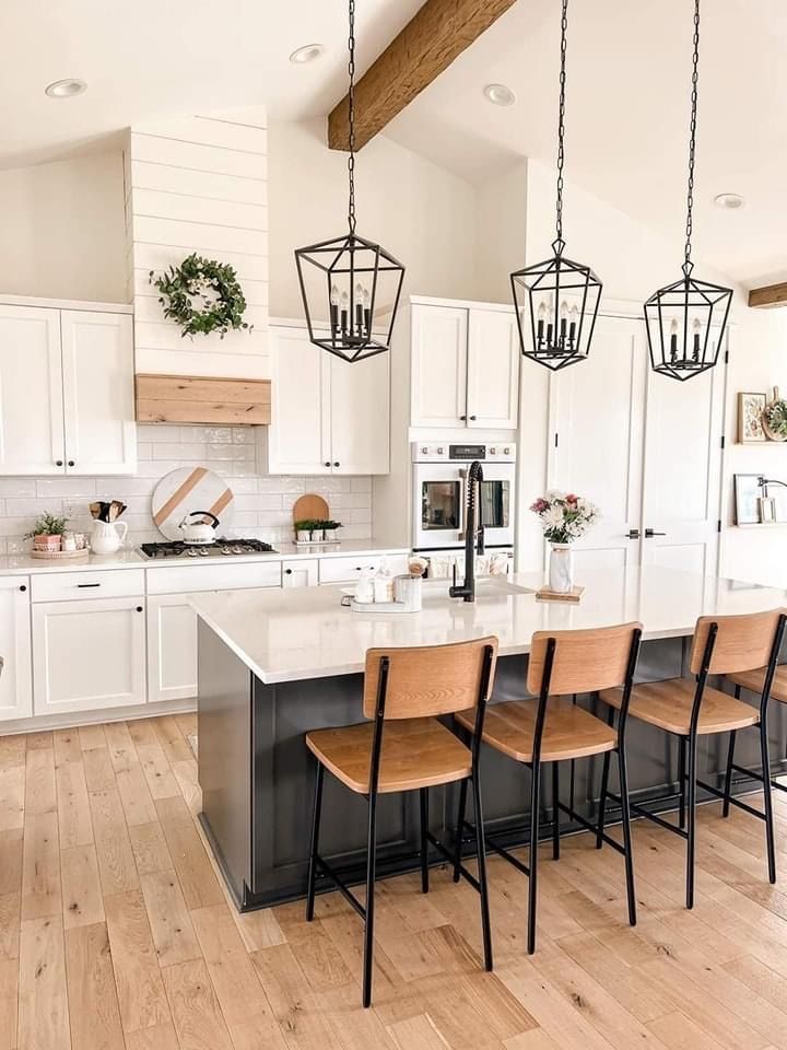 Modern kitchen with white cabinetry, a dark gray island, wooden stools, and three black lantern-style pendant lights.