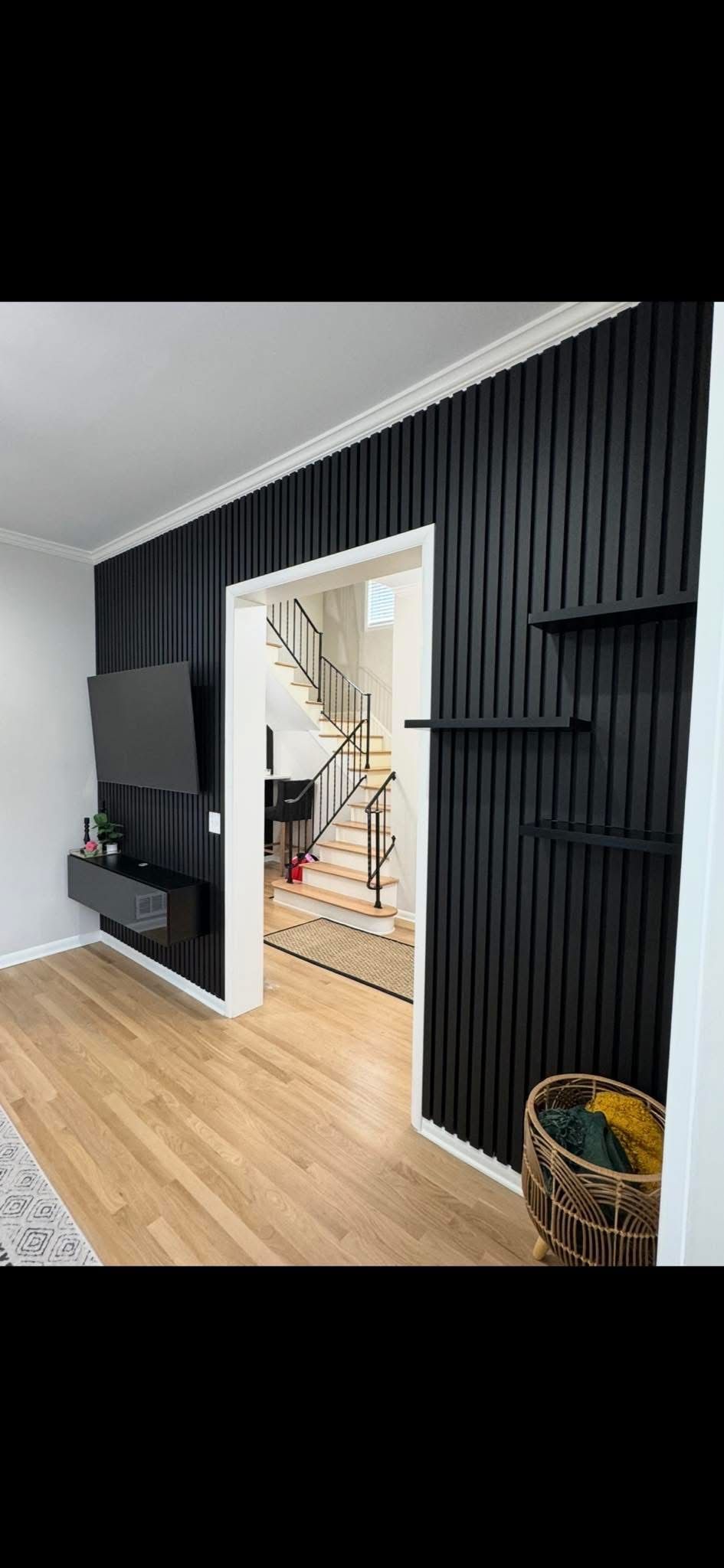 A black vertical-slat accent wall surrounds a doorway, featuring a floating TV console and two small wall shelves.