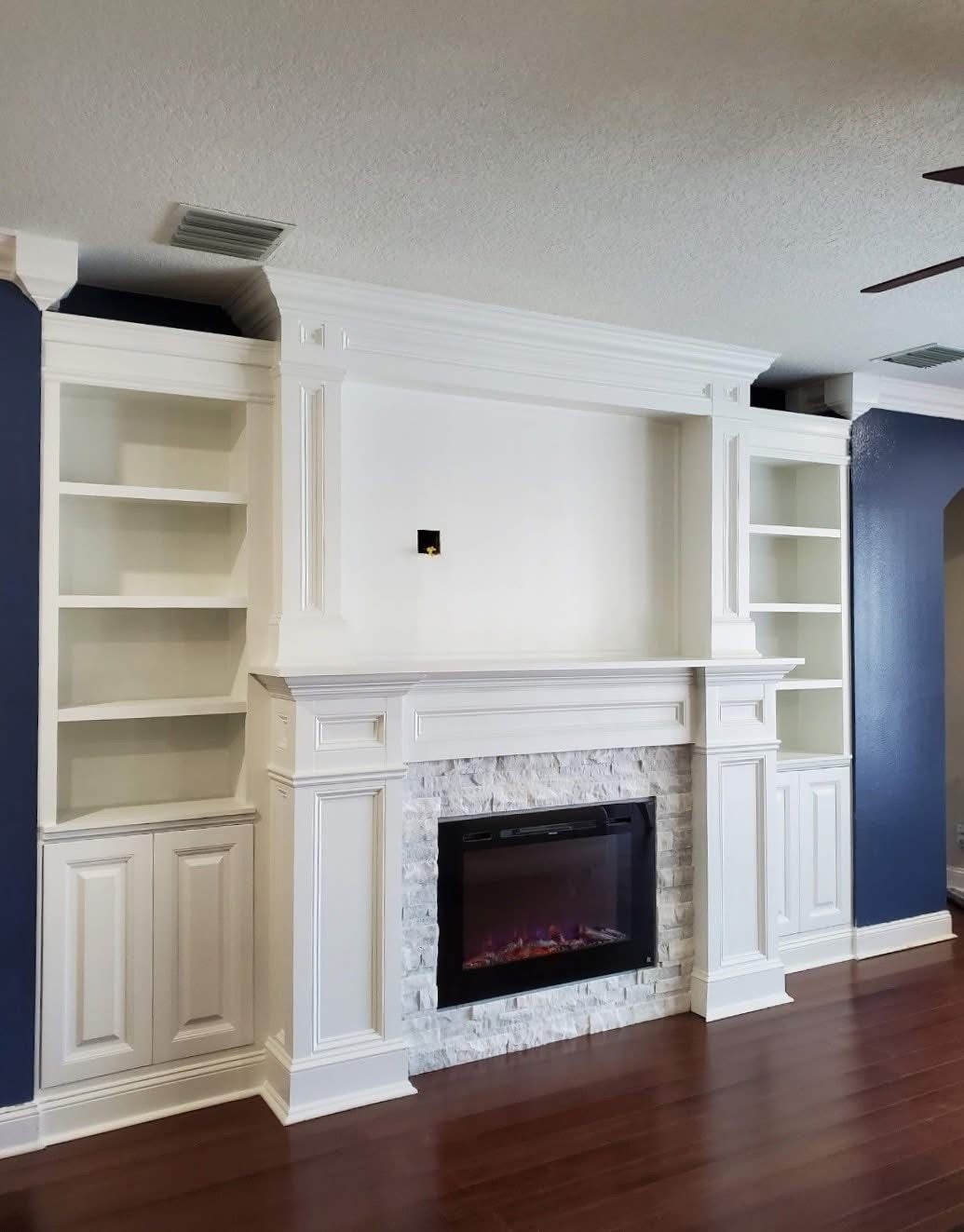 A white fireplace mantel with built-in bookshelves against a navy blue wall in a room with dark wood flooring.