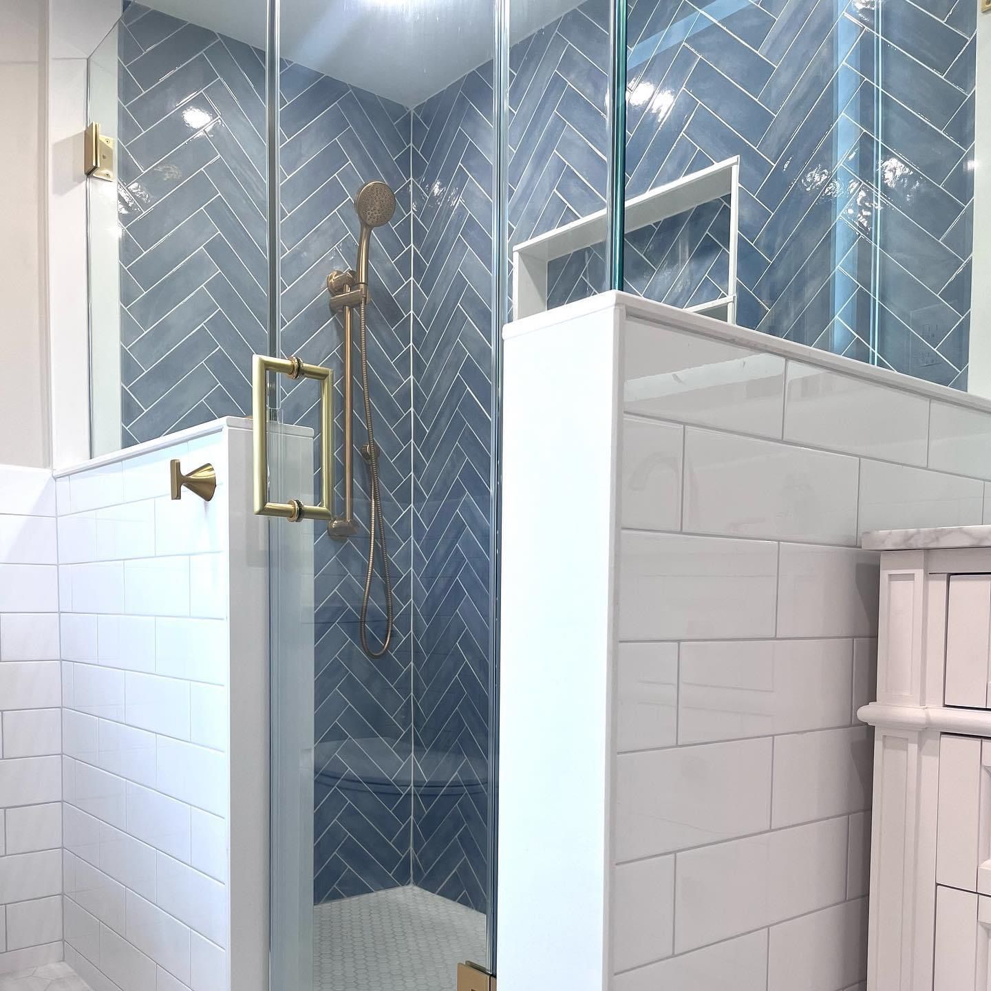 A shower with blue herringbone tiles, brass fixtures, and white subway tiles on the surrounding half-walls.
