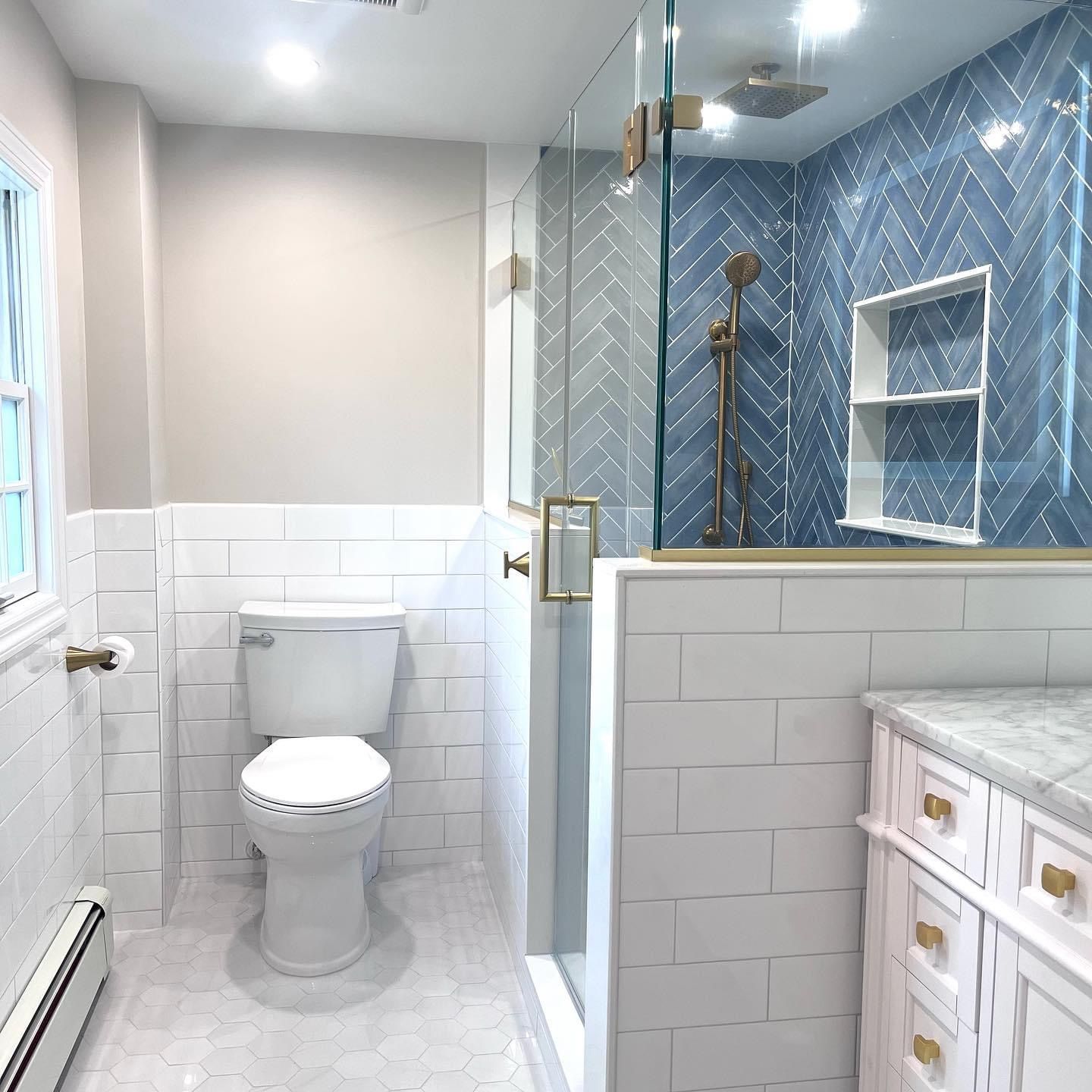 A modern bathroom featuring a white toilet, a walk-in shower with blue herringbone tile, and a white marble-topped vanity.