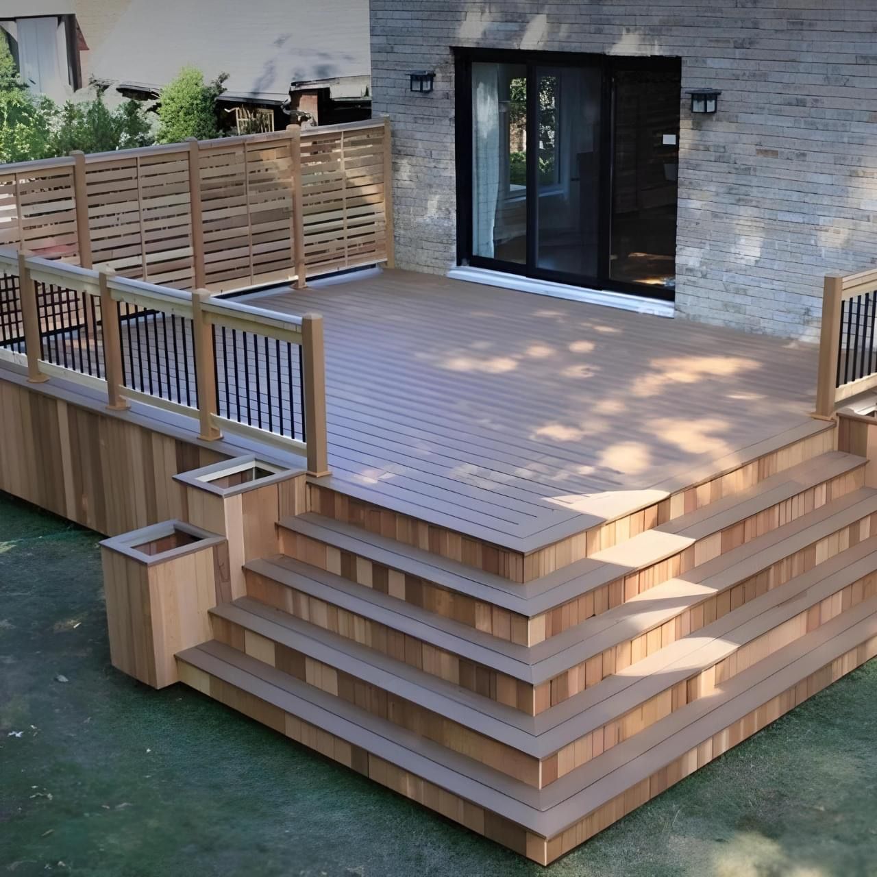 A raised, brown composite deck with wooden stairs, integrated planters, and railing attached to a house with a stone wall.