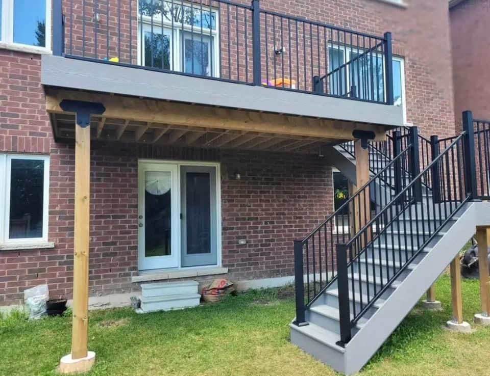 A raised wooden deck with black railings and a staircase leading down to a brick house exterior.