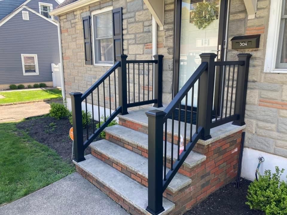 Stone steps with black metal handrails leading to the front door of a house with a brick base.