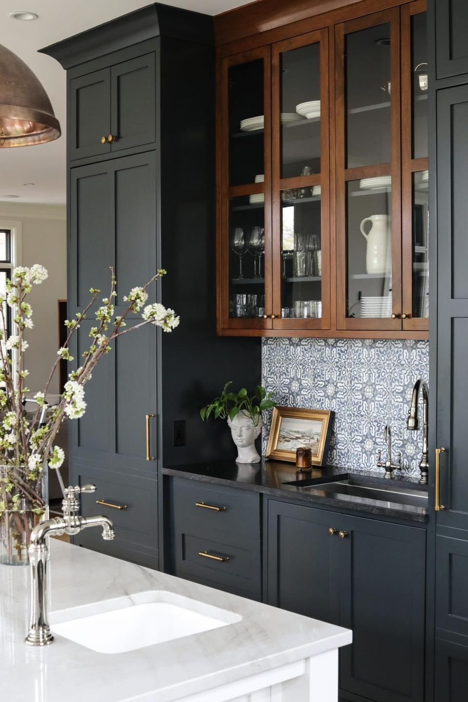 A kitchen featuring black cabinets, a wood-toned glass-front cabinet, a white marble island, and blue patterned backsplash.