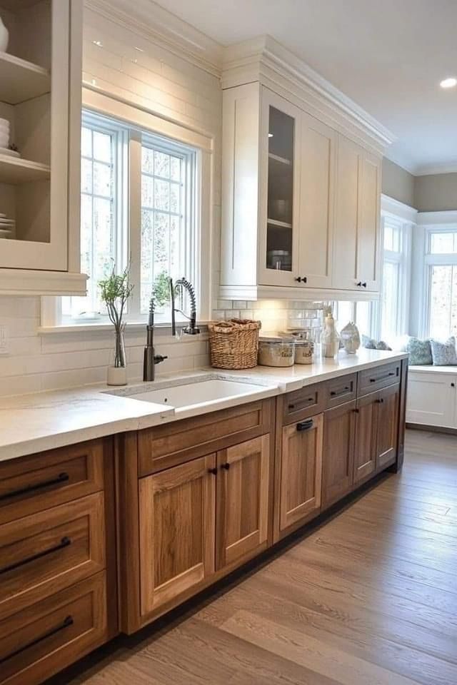 A bright kitchen with white upper cabinets, natural wood lower cabinets, white countertops, and a farmhouse sink.