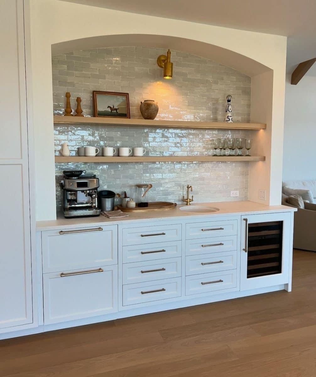 A white kitchen wet bar with an arched alcove, subway tile backsplash, wooden shelves, a coffee station, and wine cooler.