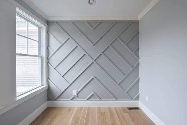 A room interior featuring a grey feature wall with a symmetrical, geometric wood slat pattern, hardwood floors, and a window.