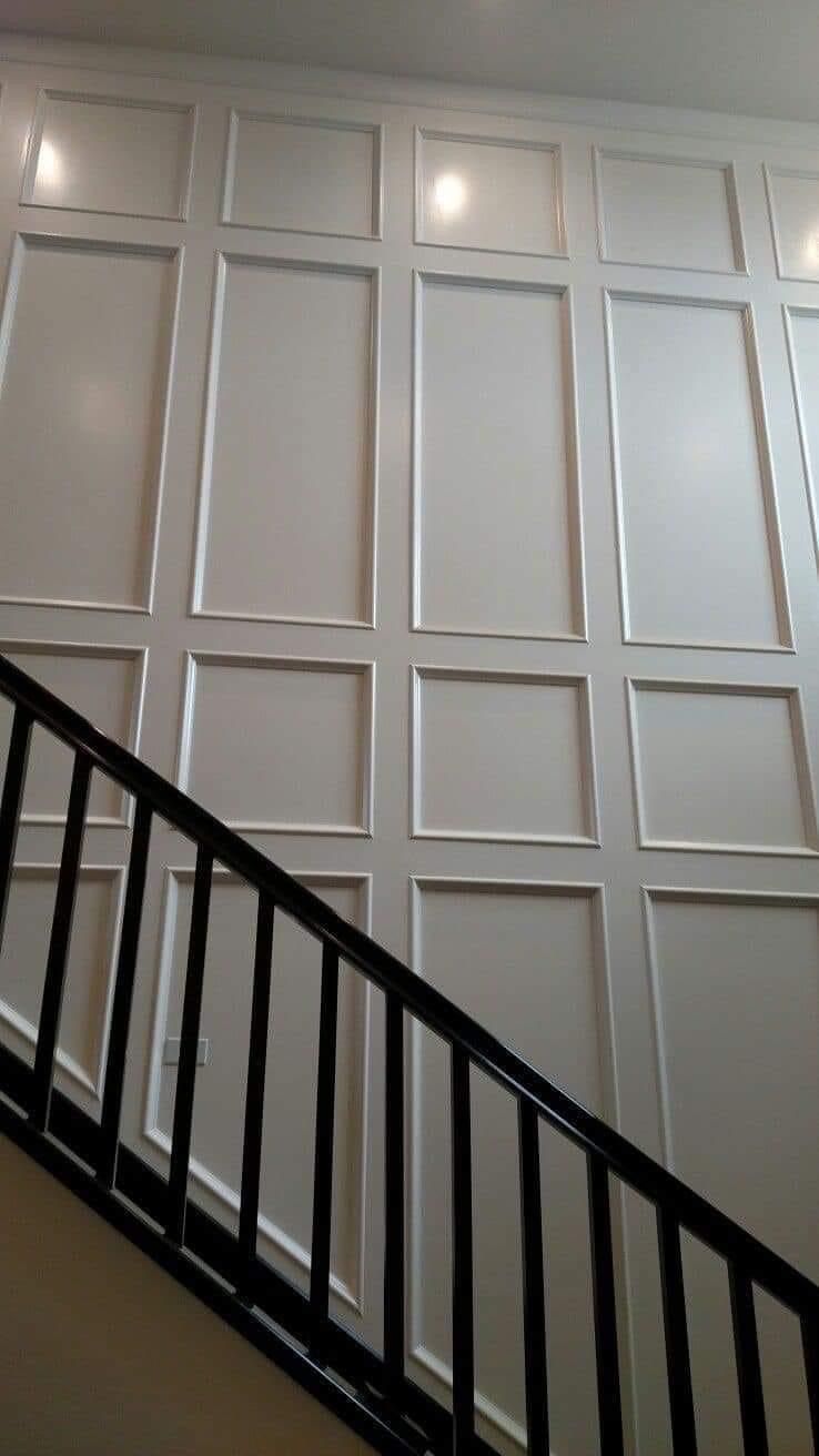 A white wall with decorative rectangular molding above a staircase with a black railing.